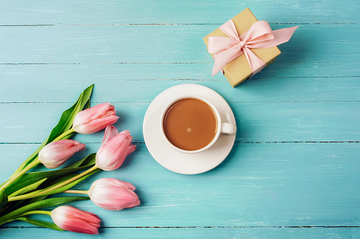 Pink tulips, a cup of coffee and gift in a box on a turquoise wooden table. Spring festive background, top view, flat lay.