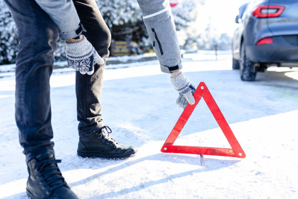 istock Driver setting up warning sign triangle on cold winter day. Broken car in the background. Road assistance and help concept. 1995501380