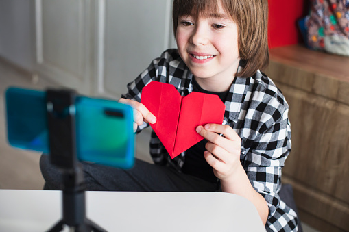 Young influencer filming vlog for his channel. Happy boy makes video for his followers online. Craft vlog. How to make origami - tutorial.  Valentine's day.