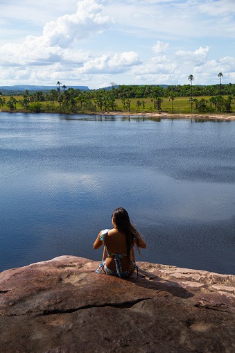 adult female in swimwear sitting on edge of rock in Salto El Sapo waterfall with beautiful view of Canaima lagoon, Carrao river, Canaima National Park, Venezuela