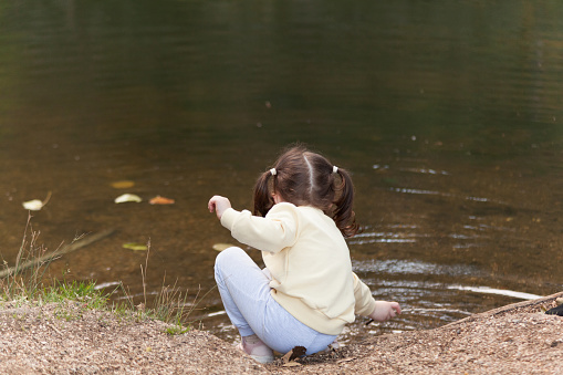 Little girl sitting on the bank of a river and looking at the water