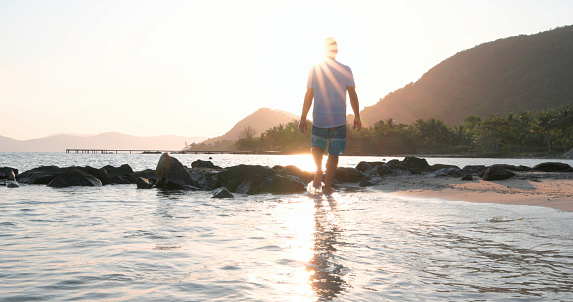 Mature man explores beach as sun rises over distant mountains