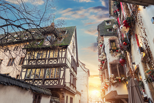 Scenic sunset view Christmas Strasbourg city street decorated Xmas toy ribbon tree beautiful warm dusk sky. Traditional Alsatian half-timbered fachwerk houses on old medieval european town center