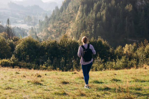istock 30s Girl with backpack on mountain peak with green grass looking at beautiful mountain valley in fog at sunset in summer. Landscape with sporty young woman, rear view. Full body 1995627672