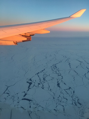 View past airplane wing lit by morning light to pack ice below