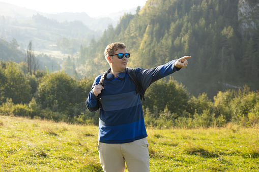 Men pointing finger on mountains background. Young male with backpack hiking in nature.