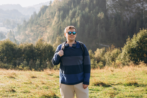 Men hiker with backpack posing at mountain peak. Travel and active lifestyle concept. 30s male enjoying valley view from top of a mountain, outdoor activities. Freedom concept