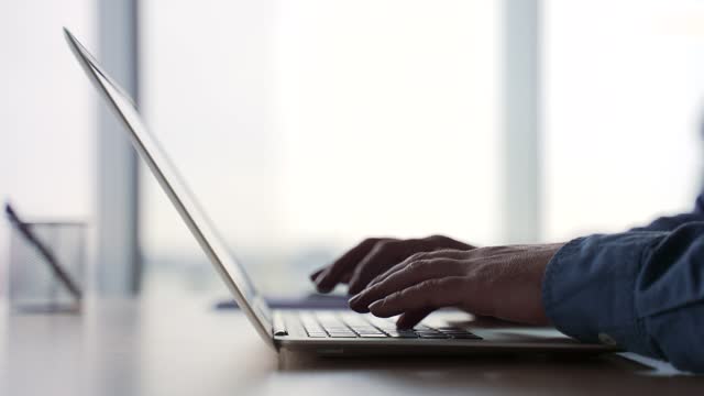 Side view. Silhouette. Close up of male hands typing on a laptop keyboard. Businessman or IT programmer