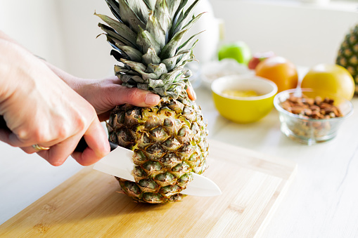 Top view of fresh pineapple with tropical monstera leaves on gray background.