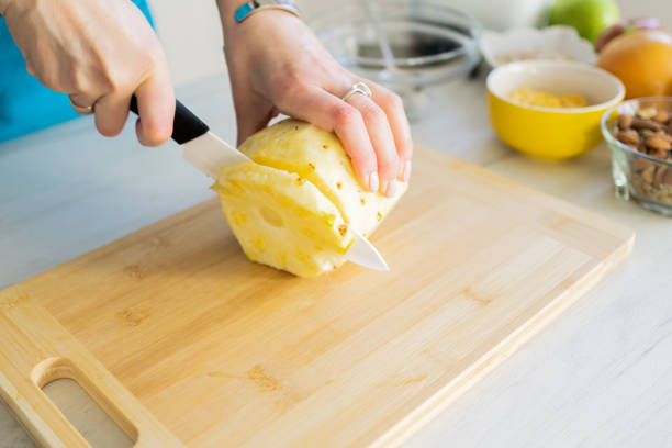 istock Healthy ingredients for tasty breakfast. Pineapple, cereal, grapefruit, apple. Woman's hands cutting fresh pineapple. 1995699063