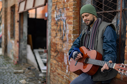 Image of Young Homeless Man Living in Poverty Playing the Guitar to Sing a Song on the Street. Homelessness Social Issues Concept. Living in the Streets.