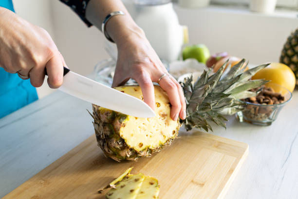 istock Healthy ingredients for tasty breakfast. Pineapple, cereal, grapefruit, apple. Woman's hands cutting fresh pineapple. 1995706428