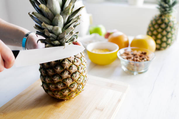 Healthy ingredients for tasty breakfast. Pineapple, cereal, grapefruit, apple. Woman's hands cutting fresh pineapple.