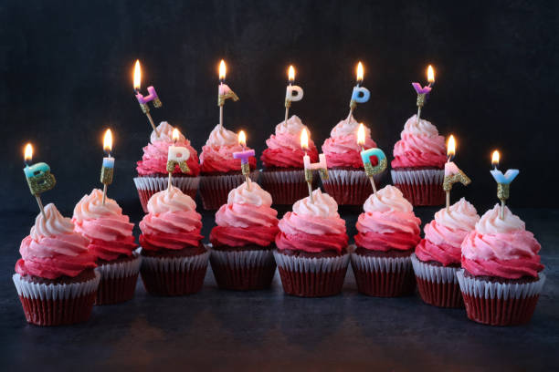 紙ケーキケースに入った自家製の赤いベルベットのカップケーキの2列のクローズアップ画像は、お誕生日おめでとうと綴り、オンブル効果ピンクバターアイシングパイプ渦巻き、黒い背景、