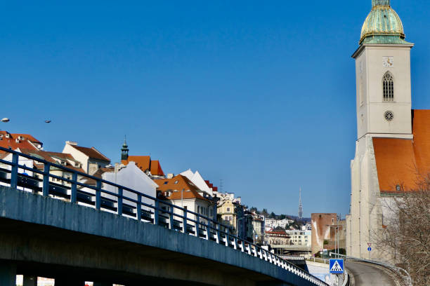 A main access road to Bratislava passes between a residential zone on the left and St. Martin's Cathedral on the right. The Kamzik TV Tower can be seen in the distance.