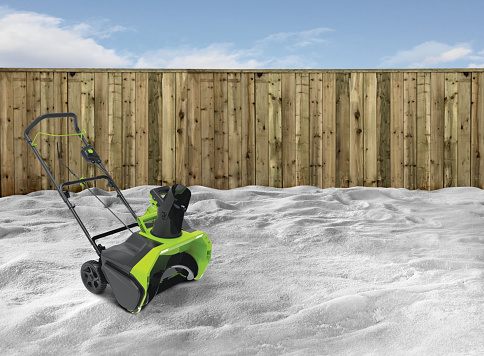 Snow blower in a backyard with snow and wood fence