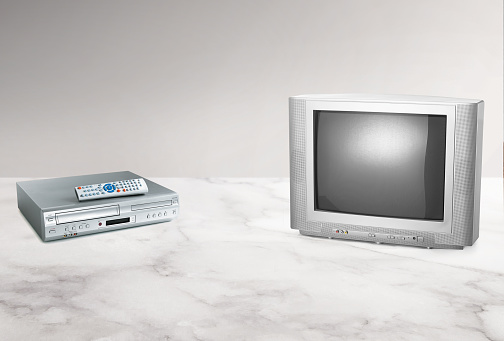 Retro old style tube tv and a VCR player with a remote control on a white marble counter top