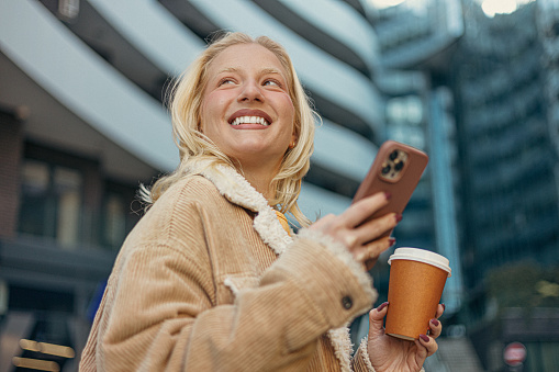 Photo of a young woman texting, sipping coffee-to-go and enyjoing city