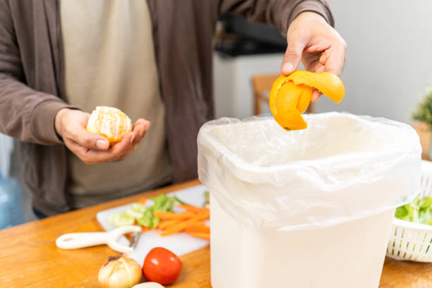 istock Ecology compost supply Kitchen waste recycling composter environmentally friendly. The young man throws leftover fruit peel and vegetables reduce waste 1995801197