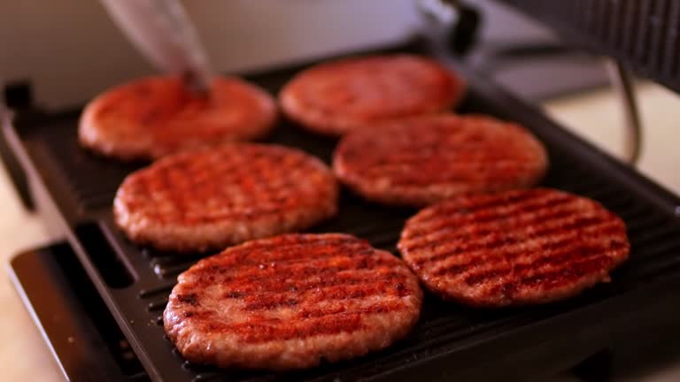 a woman fries hamburger patties on an electric grill. There is a grill in the kitchen. High quality FullHD footage