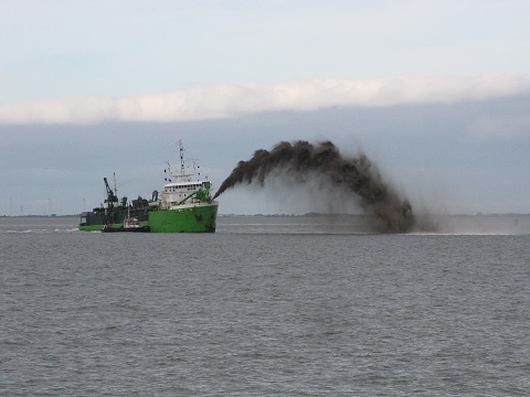 a green trailing suction hopper dredger is rainbowing at the western scheldt sea closeup