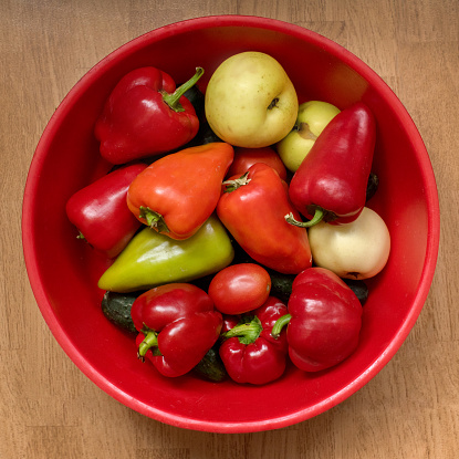 Fresh vegetables in a heap in a bowl on a wooden background, home grown sweet red, yellow, green peppers