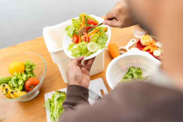 istock Ecology compost supply Kitchen waste recycling composter environmentally friendly. The young man throws leftover fruit peel egg shell and vegetables reduce waste 1995819103