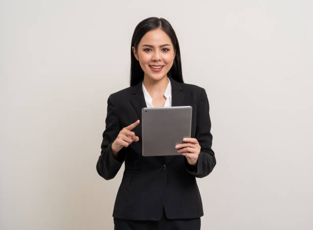 istock Attractive elegant young asian business woman using digital tablet standing on isolated background. Happy young latin female formal black suit holding tablet gadget working service with customer 1995821800
