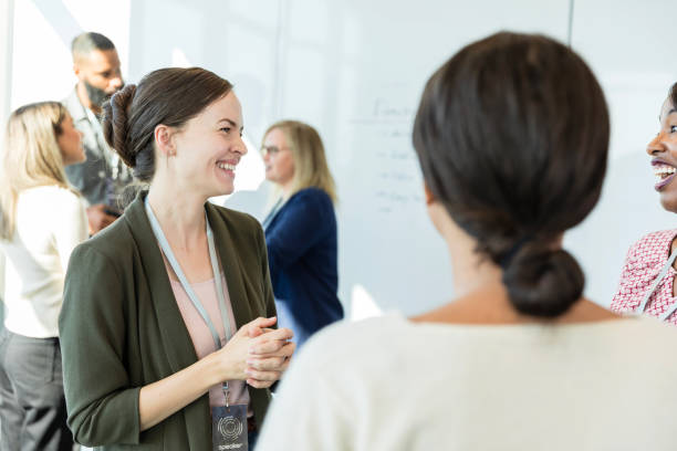 istock Female seminar presenter smiles while chatting with unrecognizable businesswomen 1995828622