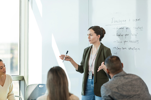 The young adult female CEO speaks to a multiracial group of employees about developing a vision for their workplace.