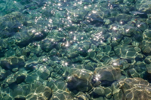 Green sea water with shiny sparkles and rocks underwater