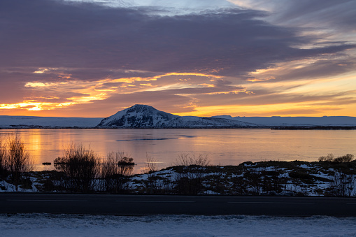 Colorful cloudy sky during the sunset. Lake with a clam water and on a horizon a hill, partly covered by snow. Myvatn, Iceland.