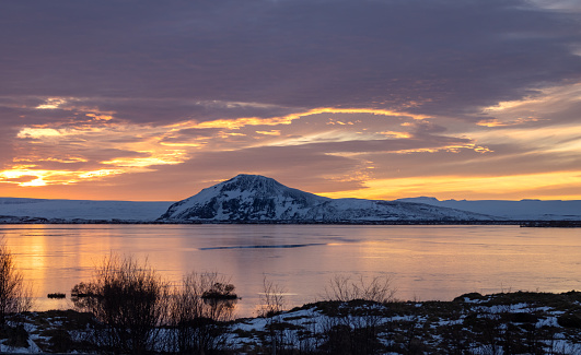Colorful cloudy sky during the sunset. Lake with a clam water and on a horizon a hill, partly covered by snow. Myvatn, Iceland.