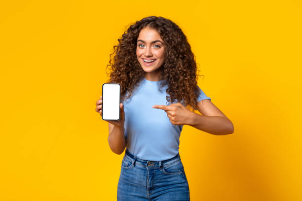 istock Cheerful woman showing smartphone screen on yellow 1995838179