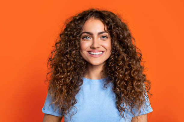 istock Curly-haired woman smiling brightly on orange backdrop 1995838183