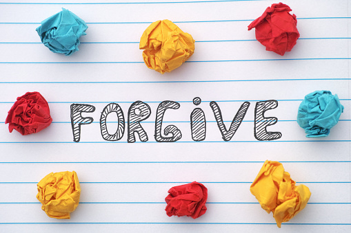 Forgive. The word Forgive written on a notebook sheet with some colorful crumpled paper balls around it. Close up.