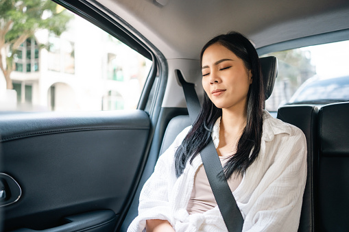 Relaxing moment of beautiful woman sleeping in car back seats with safety belt. Female happy in car while traveling on the road to destination.
