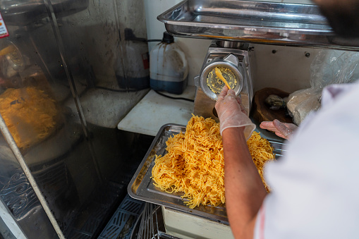 Employees in a small food business specializing in empanadas, dressed in uniform, are in the business kitchen preparing the implements they use for the day's preparation.