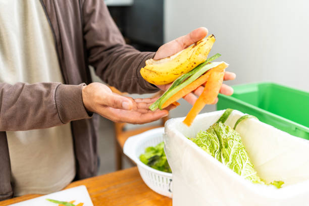 istock Ecology compost supply Kitchen waste recycling composter environmentally friendly. The young man throws leftover fruit peel and vegetables reduce waste 1995849121