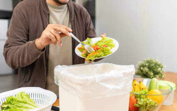 istock Ecology compost supply Kitchen waste recycling composter environmentally friendly. The young man throws leftover fruit peel egg shell and vegetables reduce waste 1995849122
