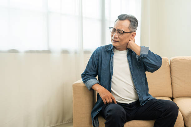 istock Old man senior has problem with structural posture He had neck and shoulder pain. Mature Massaged his neck and shoulders for relief. reduce muscle tension. Sitting on sofa couch in living room 1995849648