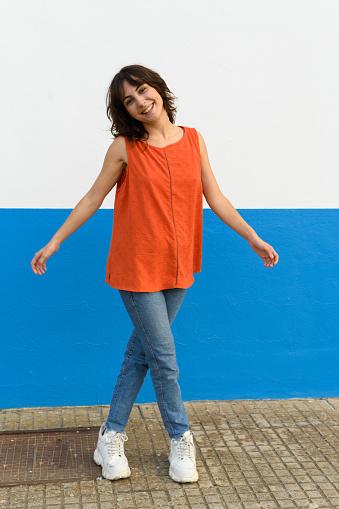 Vertical portrait of a caucasian woman posing with open arms next to an urban wall