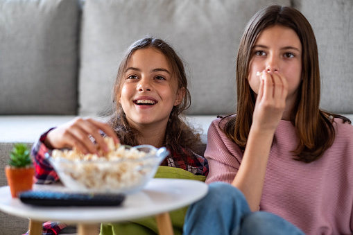 two girls are eating popcorn and watching a movie at home