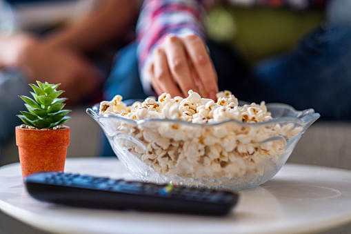a girl is eating popcorn and watching a movie at home, close up on hand