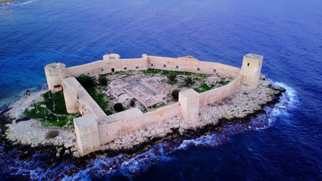 Witness the breathtaking Maiden's Castle in Kizkalesi through captivating aerial footage Explore Mersin's coastal beauty at sunset featuring archaeological area on the island with the colossal ruins