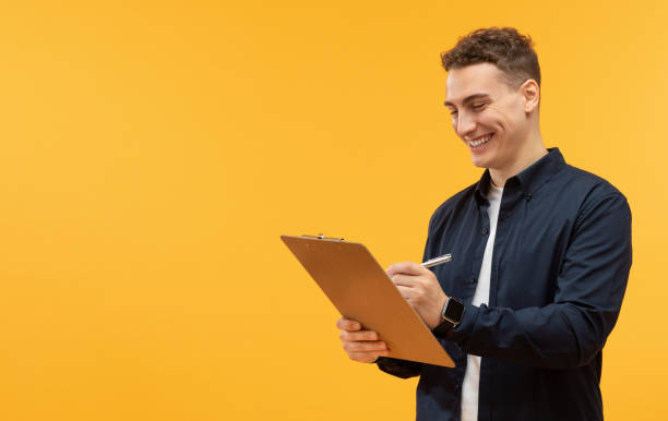 istock Happy young man taking notes in clipboard, yellow background 1995890099