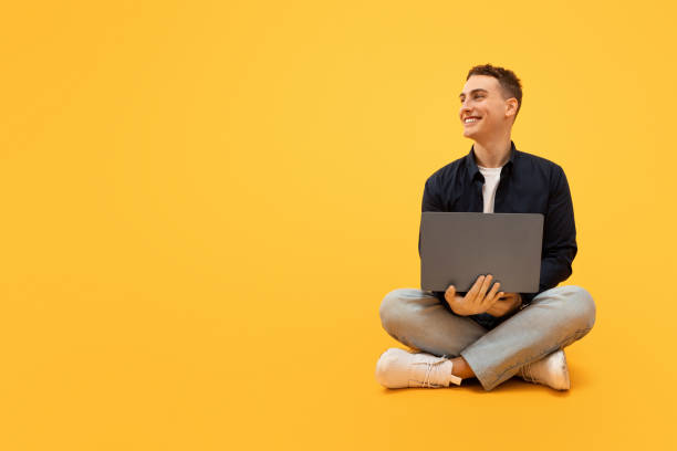 istock Positive young guy freelancer working on laptop, yellow background 1995891698