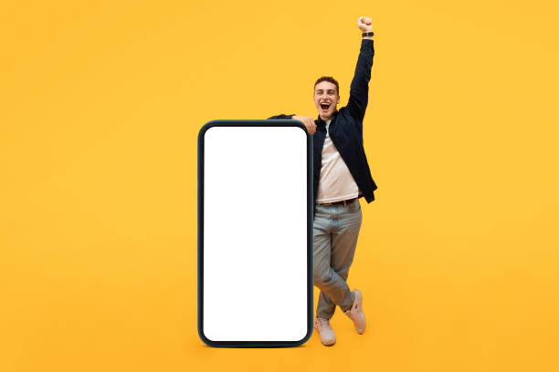 istock Cool Mobile Offer. Excited casual guy stand by big smartphone 1995891719