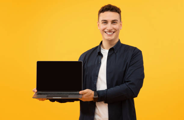 istock Happy young man holding laptop computer with black blank screen 1995892260