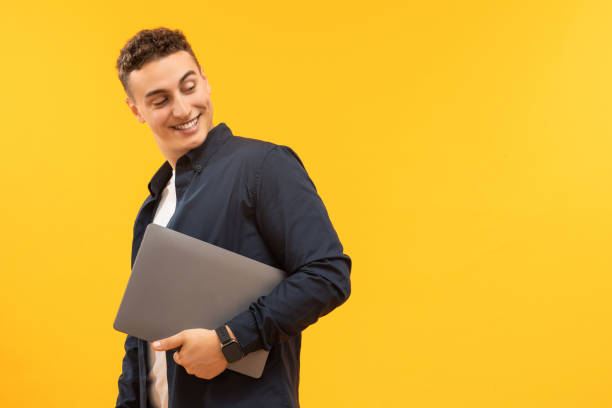 istock Happy millennial handsome man holding laptop, yellow background 1995892263